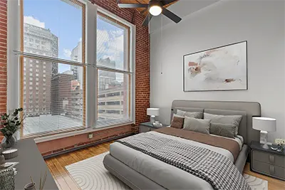 Spacious bedroom with large windows, city views, exposed red brick walls, and hardwoood floors