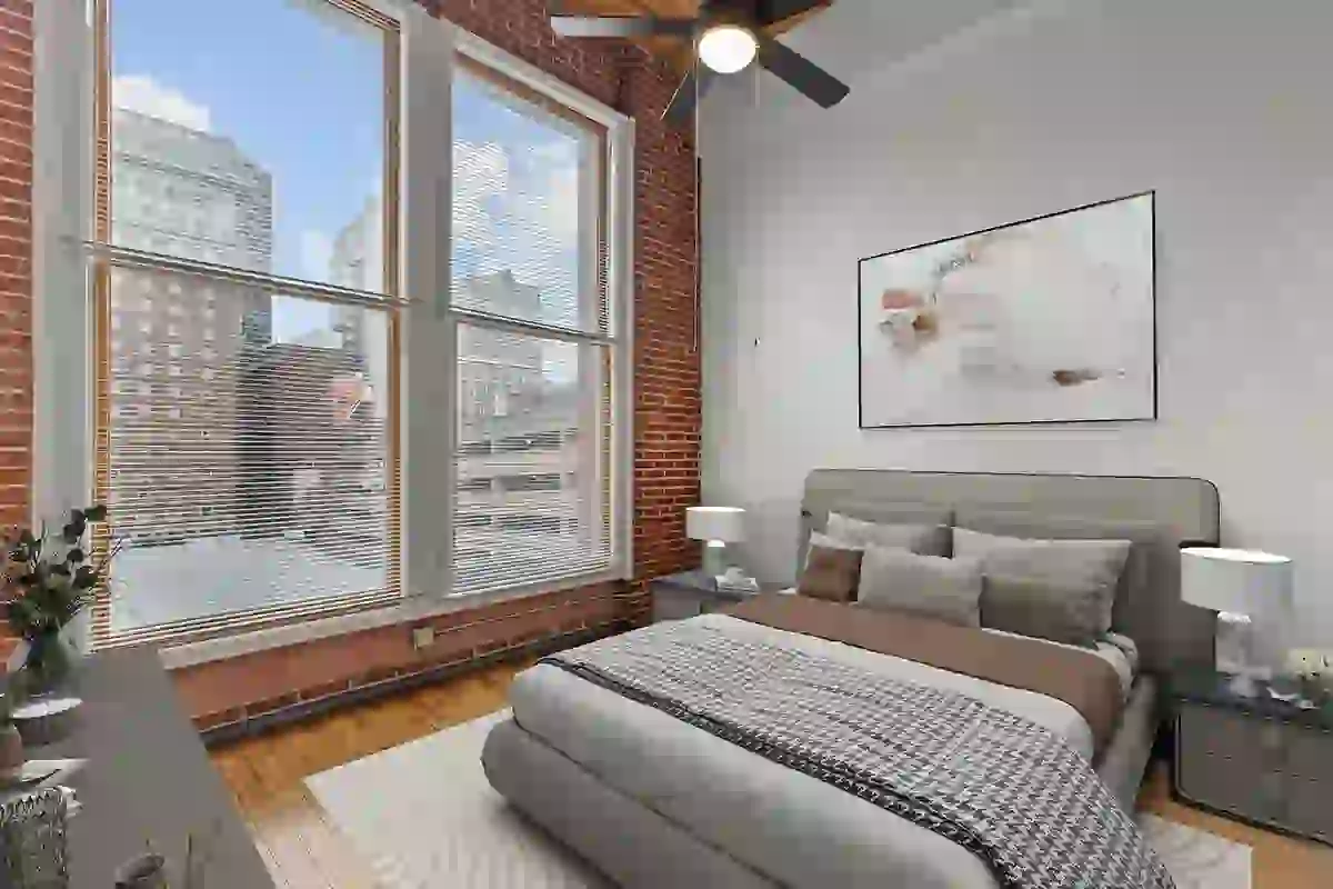 Spacious bedroom with large windows, city views, exposed red brick walls, and hardwoood floors
