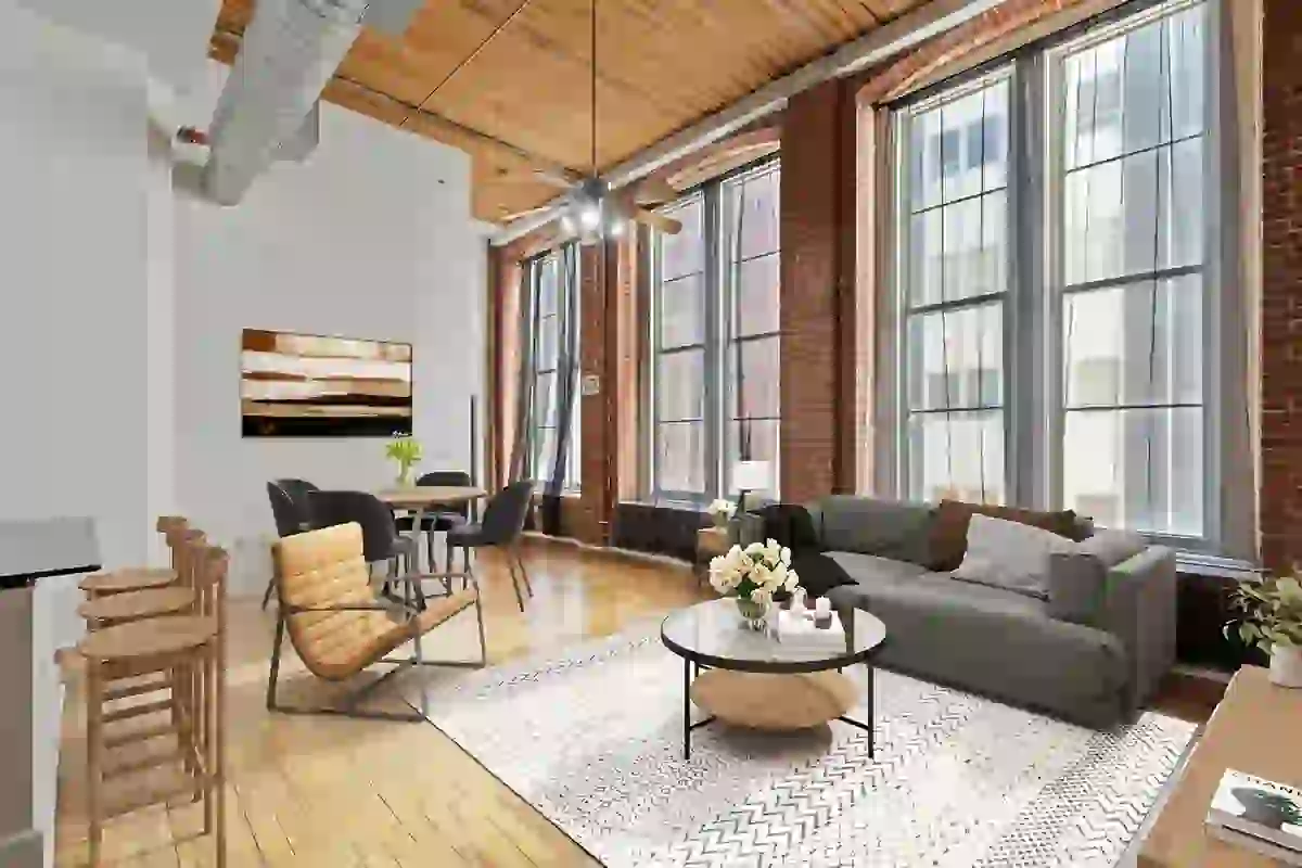 Living room in loft-style apartment with tall ceilings, large windows, exposed brick, and wood flooring