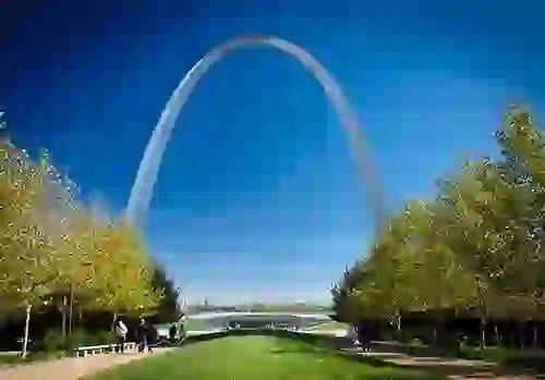 A large open green field of grass and trees at Gateway Arch National Park with the famous Arch in the background