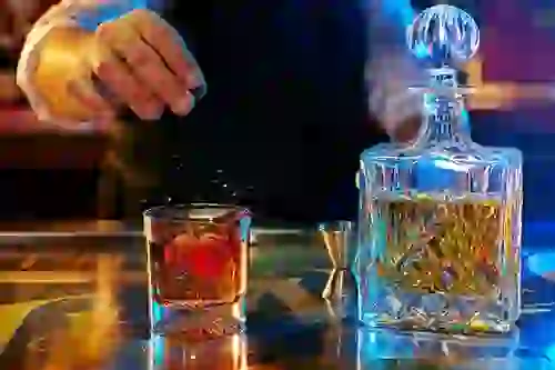 Close-up of bartender's hands preparing a craft cocktail with vibrant, moody lighting at Thaxton's Speakeasy
