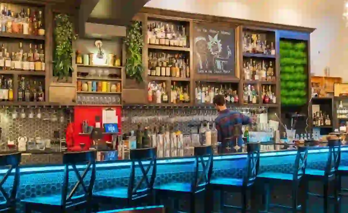 A bartender pouring a drink behind a well lit bar with shelves of bottles
