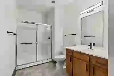 Renovated bathroom with glass shower door, gray tile floor, wood cabinetry, light countertop, and oversized vcanity mirror with even lighting