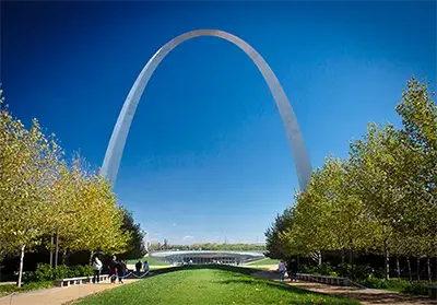 A large open green field of grass and trees at Gateway Arch National Park with the famous Arch in the background