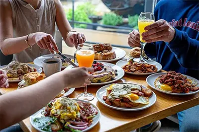 A group of friends eating several plates of food and cocktails at Rooster