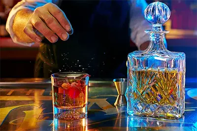 Close-up of bartender's hands preparing a craft cocktail with vibrant, moody lighting at Thaxton's Speakeasy