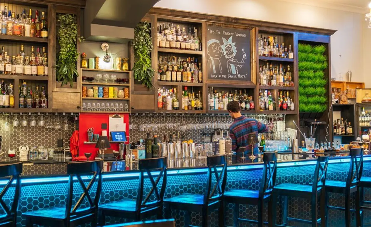 A bartender pouring a drink behind a well lit bar with shelves of bottles